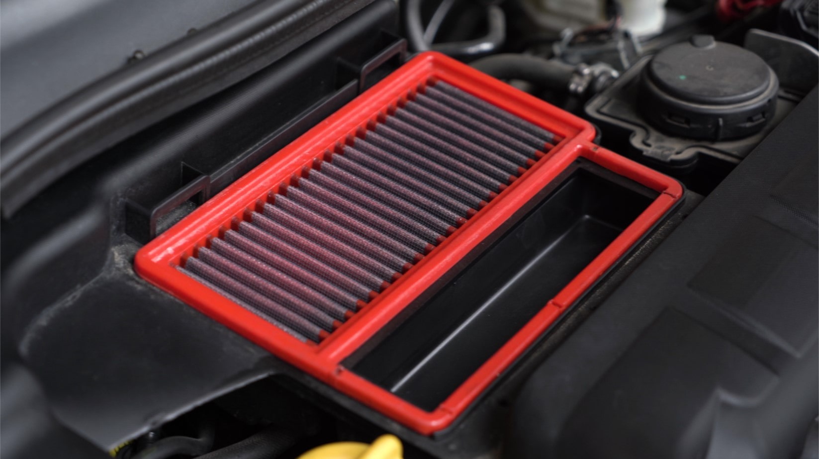 A clean red engine air filter installed in a car engine bay.